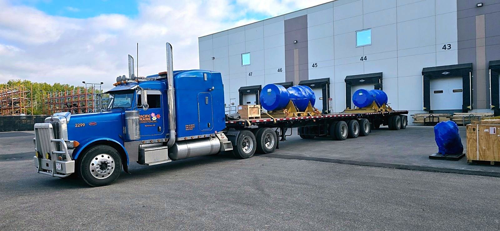 Blue Pacific Prairie Connections Peterbilt with two tanks secured on a flatdeck at a loading dock